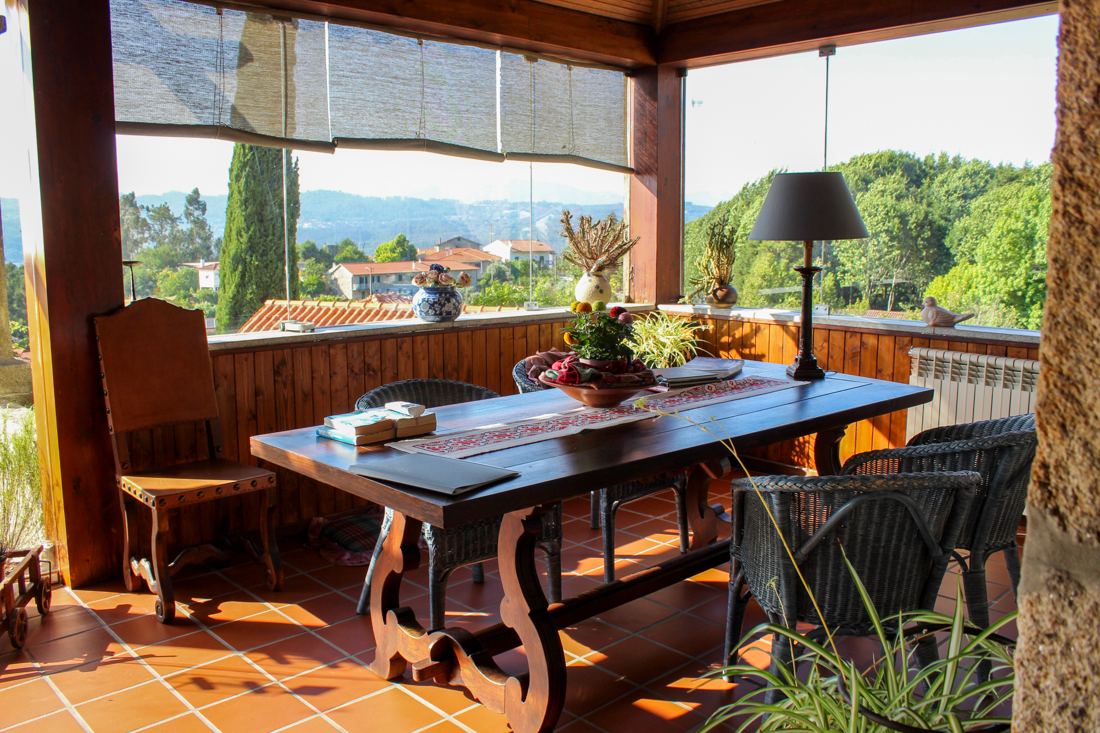 Varanda envidraçada com mesa de madeira e vista para a serra